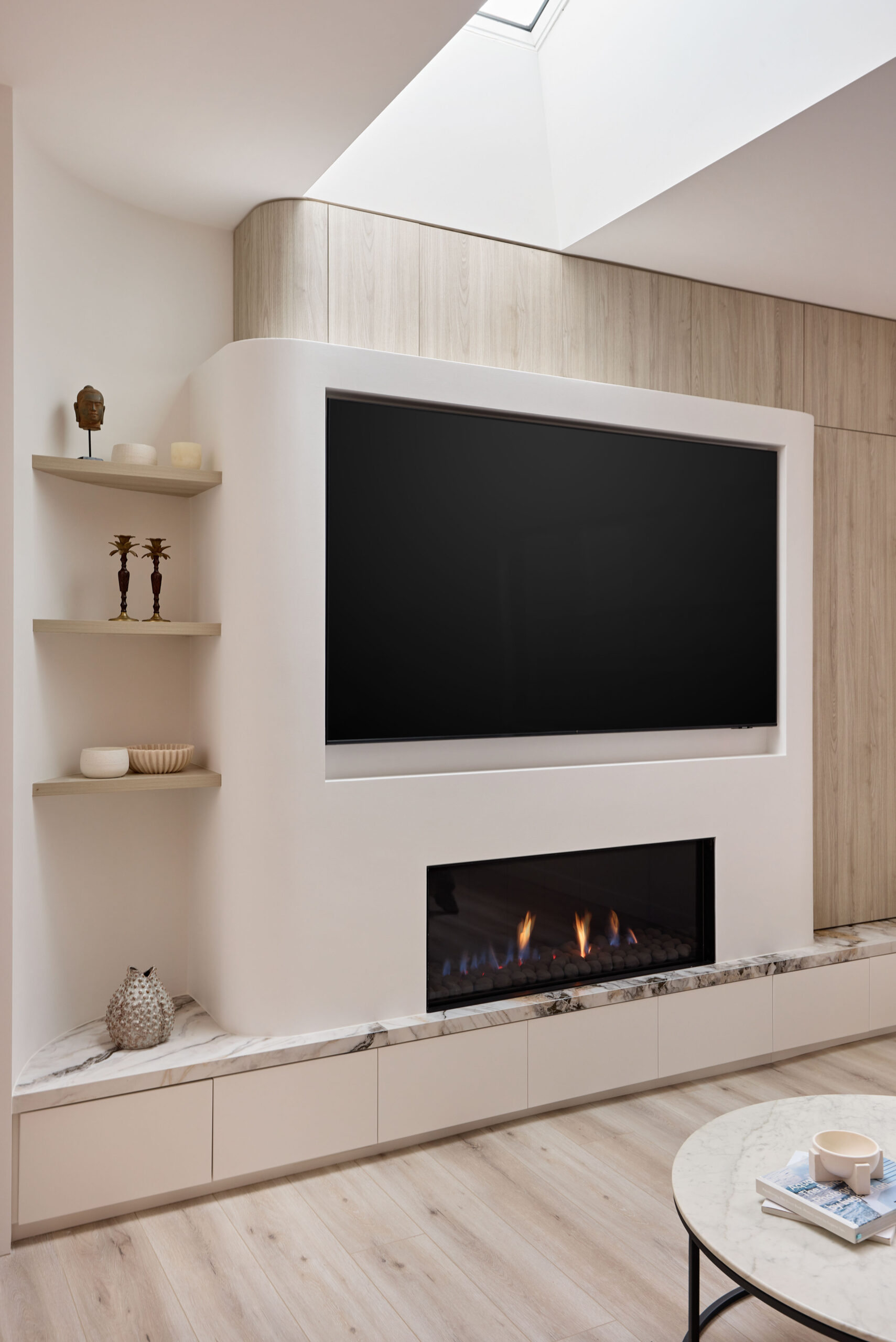 Modern living room wall unit with a large flat-screen TV above a marble-mur fireplace and light wood cabinetry.