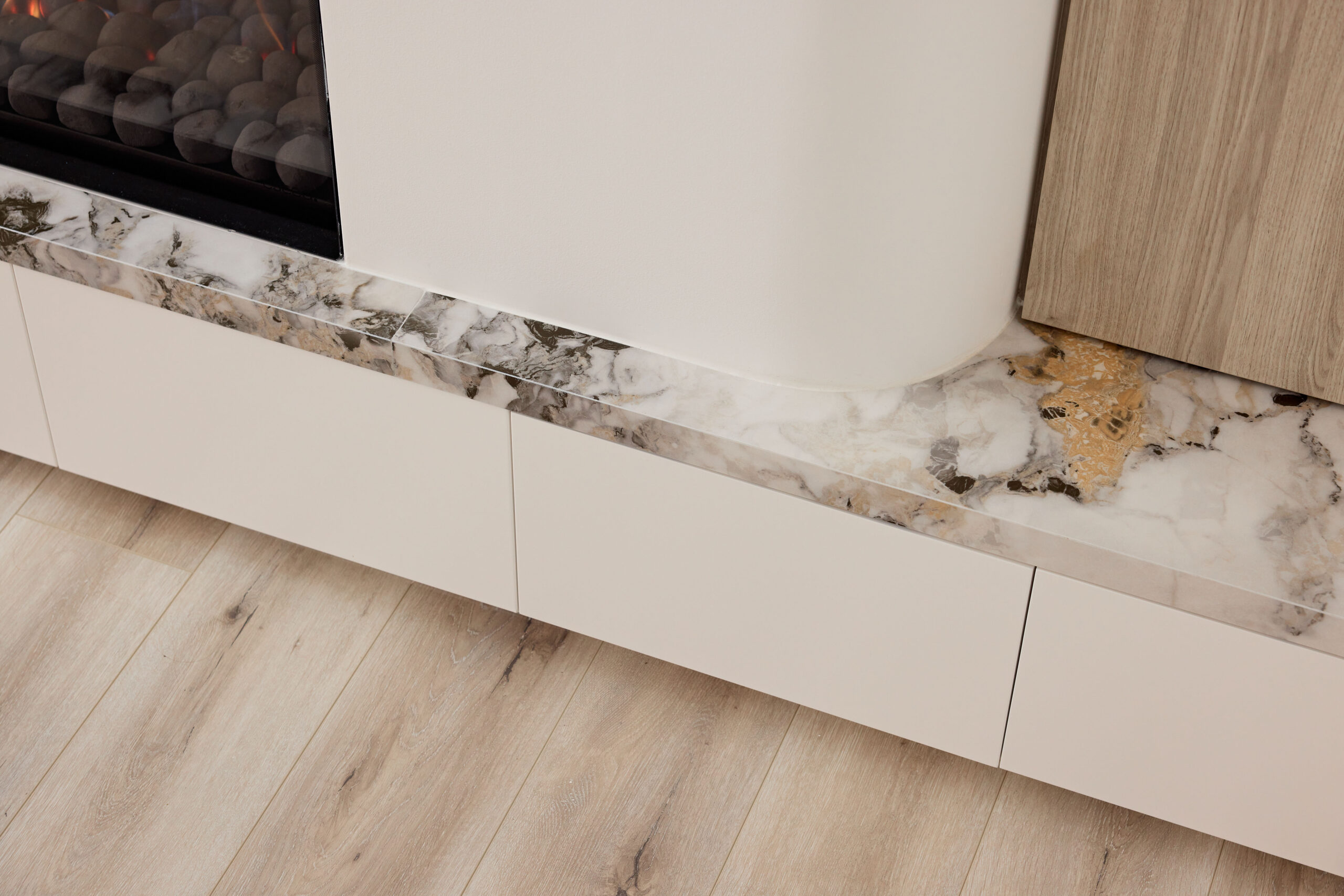 Close-up of beige kitchen cabinetry with a marble countertop and light wood floor beneath.