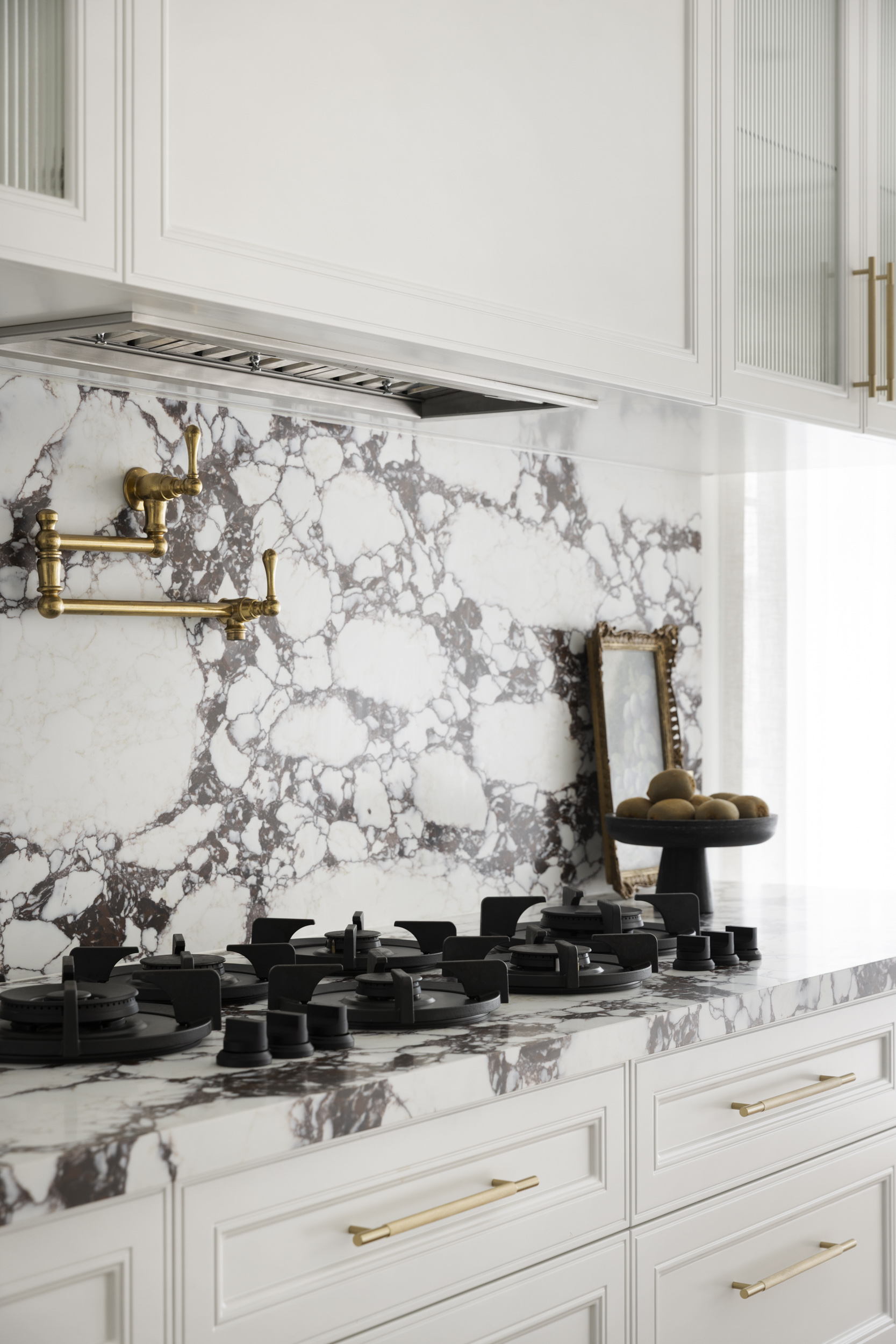 White cabinets with gold handles over a marble backsplash and a gas stove on the countertop