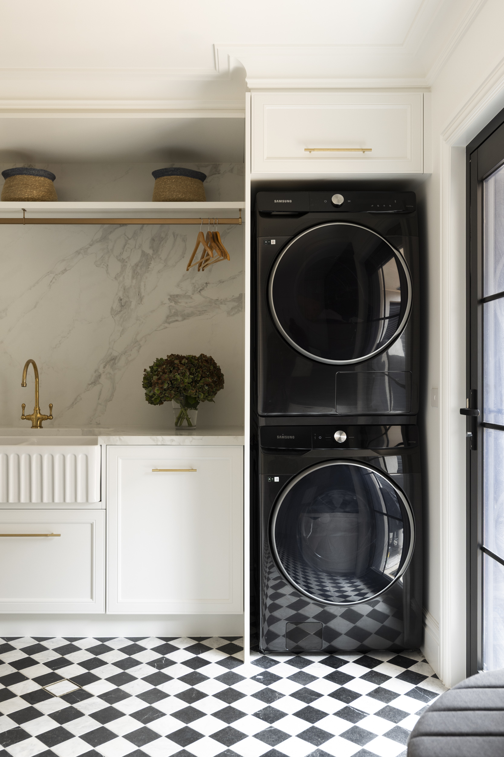Stacked black Samsung washer and dryer inside a white cabinet, with marble backsplash and gold fixtures in a laundry alcove.