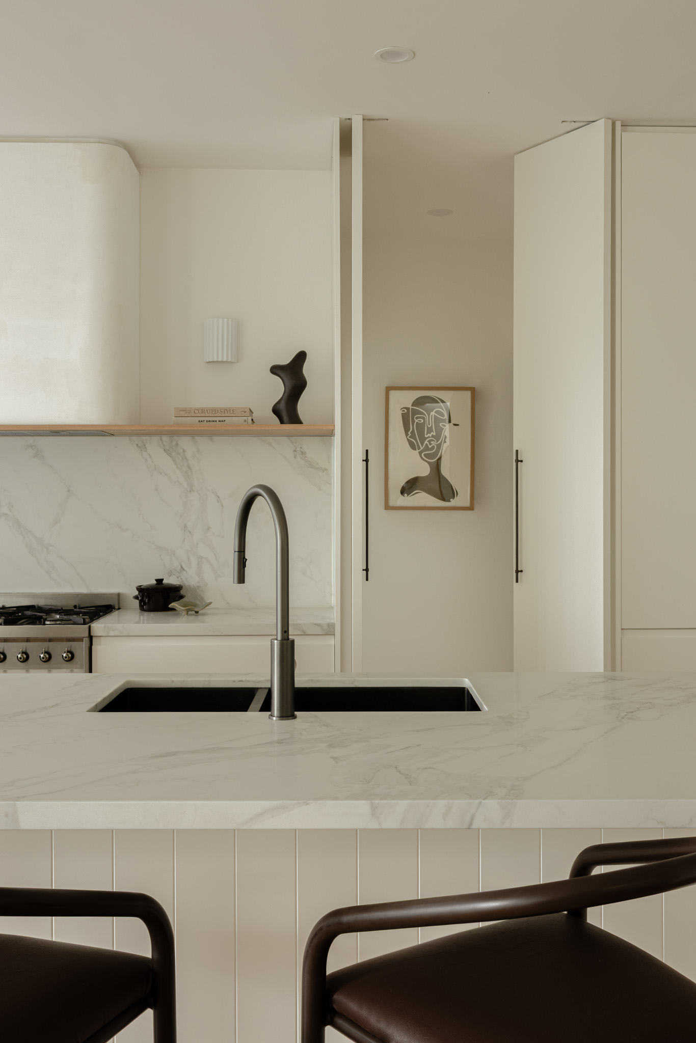 Modern kitchen with marble island countertop, stainless faucet, and white cabinets; abstract framed art on the wall.