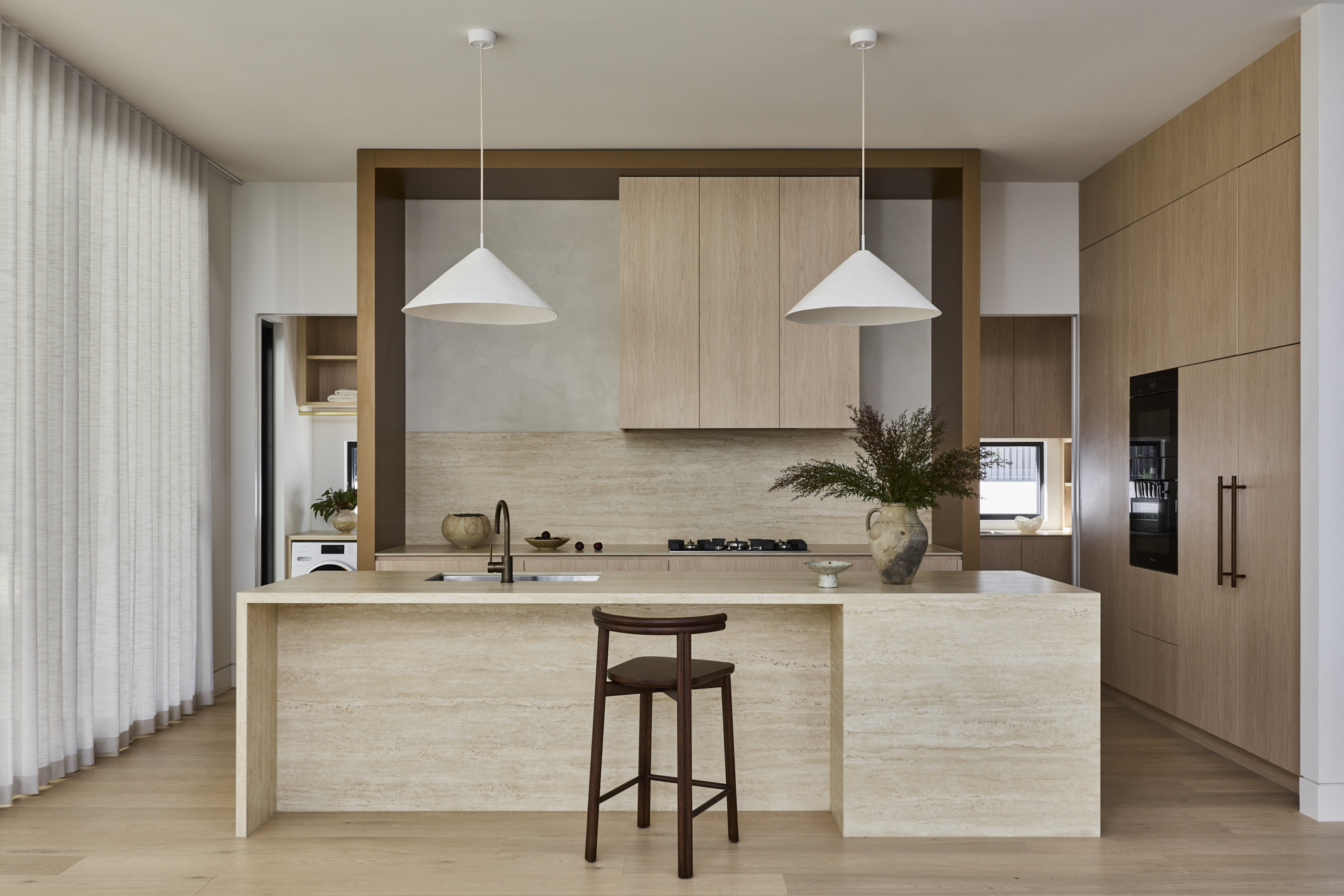 Modern kitchen with a beige stone island, light wood cabinets, and two white cone pendant lights above the center island.