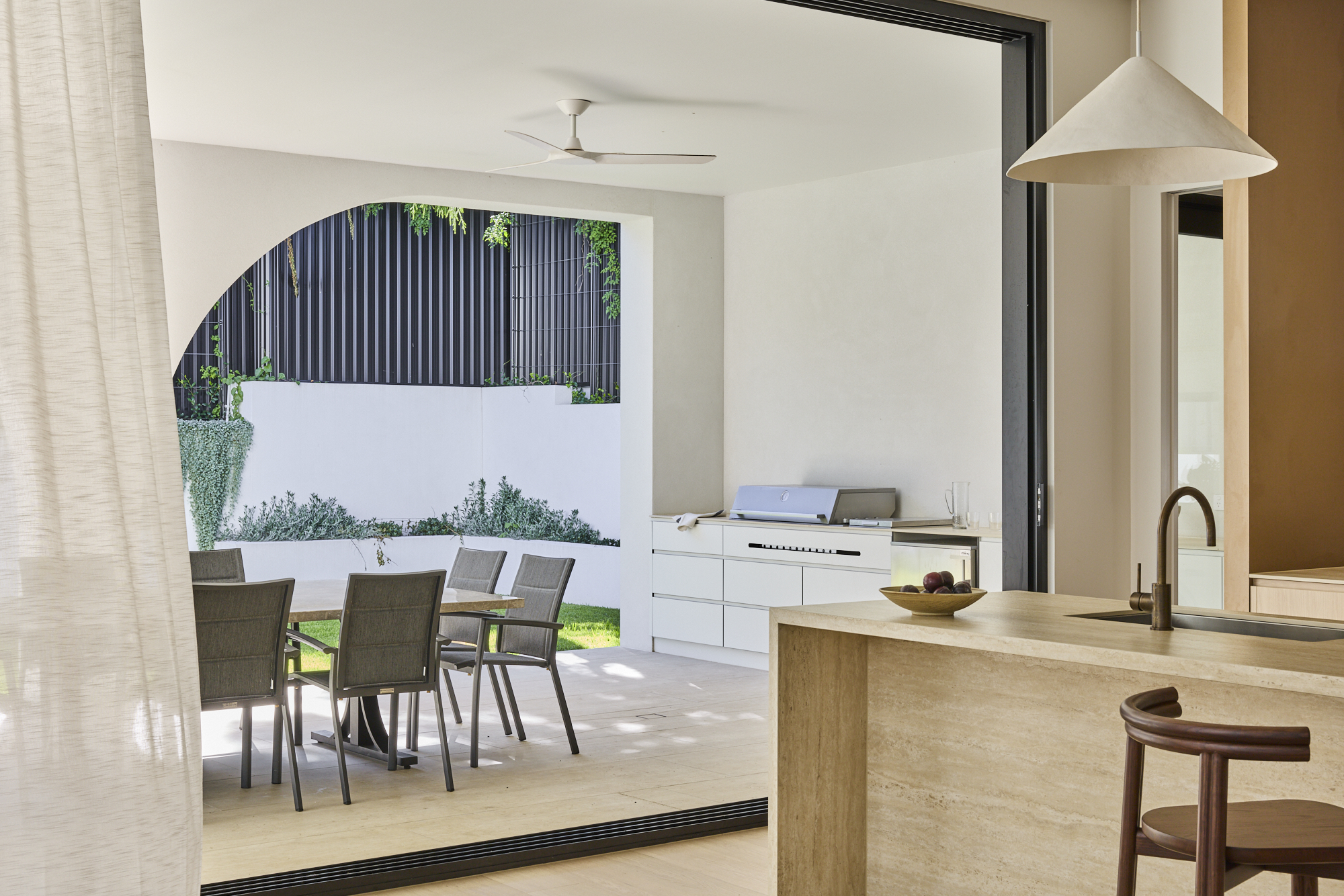Indoor kitchen opening to a covered patio with a dining table and chairs and built-in grill area outside.