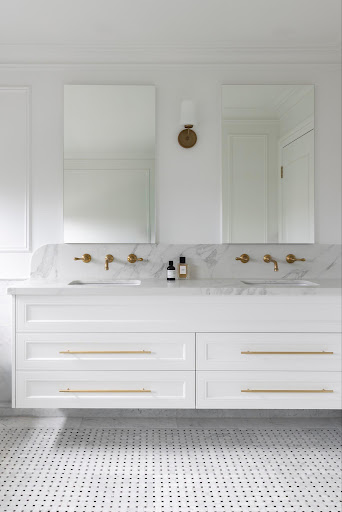 White bathroom vanity with marble countertop, two sinks, and gold faucets with two mirrors above it.