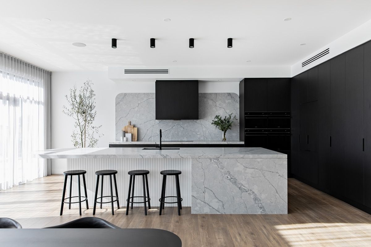 Open-plan kitchen with a marble island, black cabinetry, and four black stools.