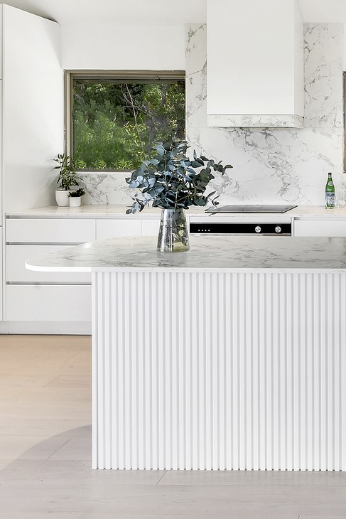 White modern kitchen with a marble island and a vase of greenery on the island.