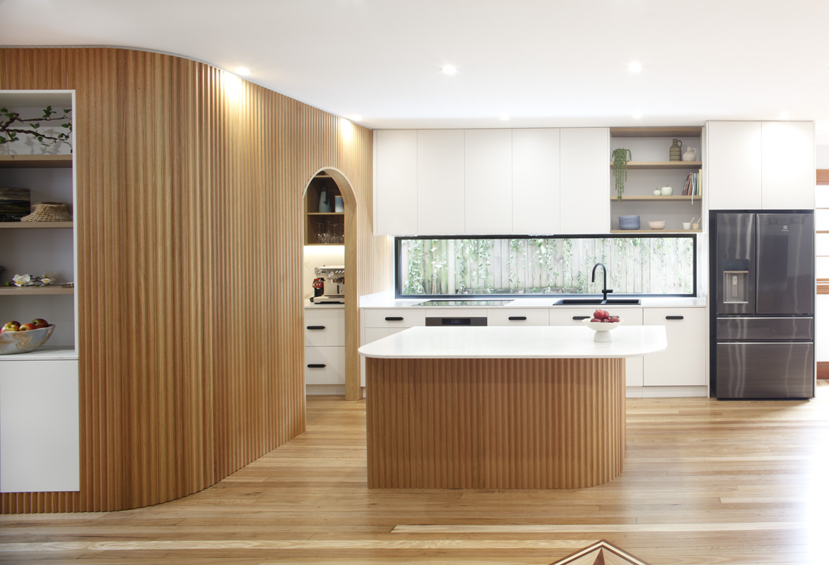 Bright modern kitchen with a curved vertical wood slat wall, white cabinets, and an island centerpiece.