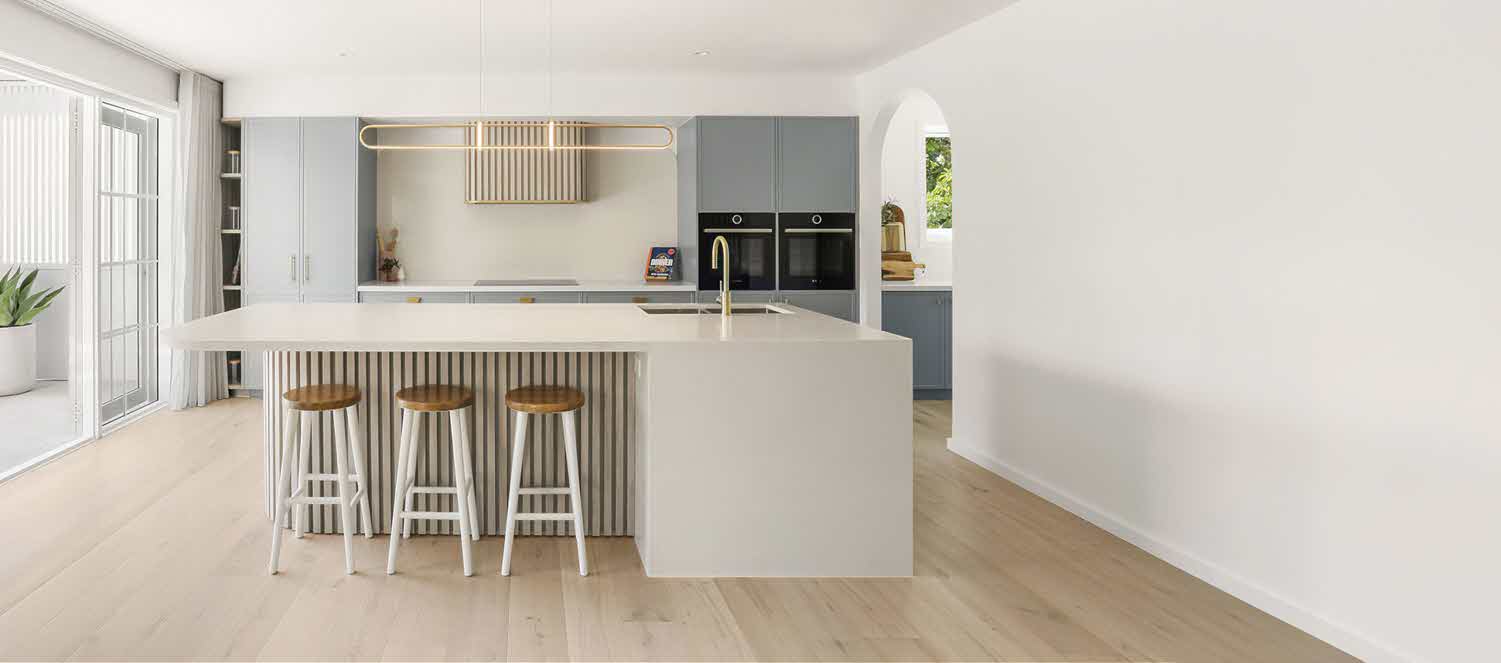 Bright modern kitchen with a white island, wooden-stool seating, and gray cabinetry throughout a sunlit room.