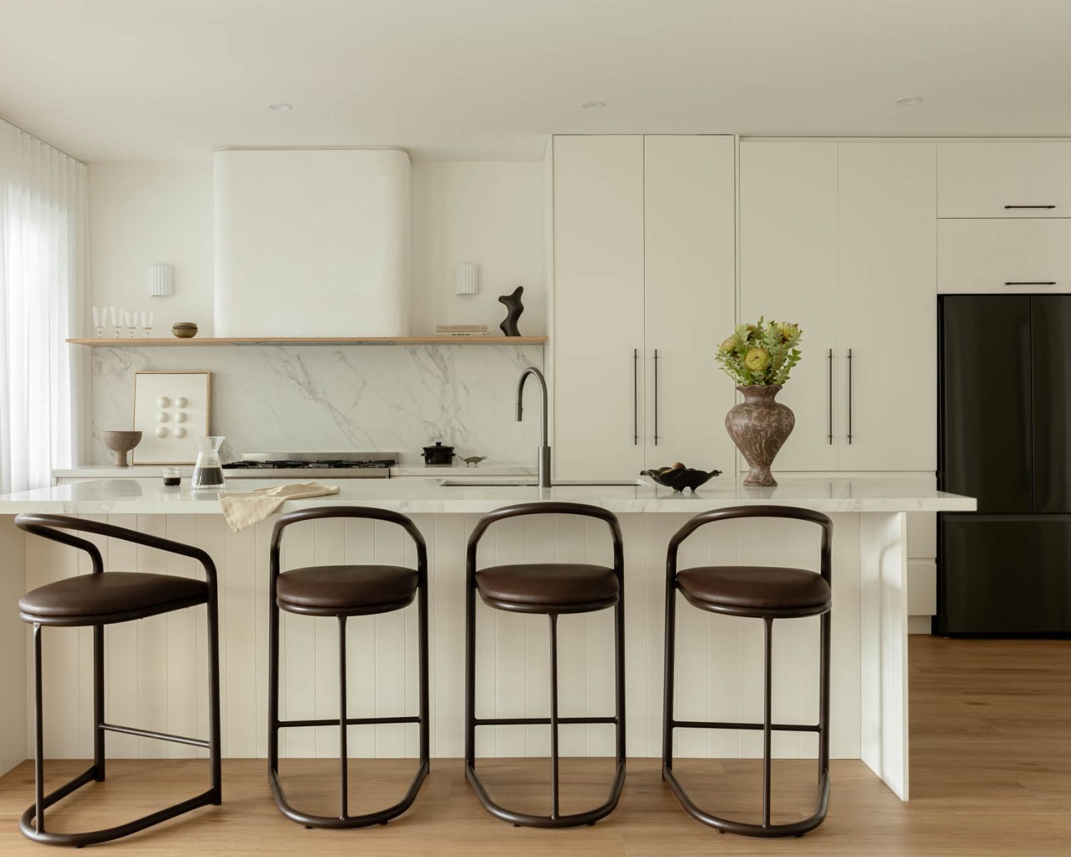 Bright modern kitchen with white cabinets, marble island, and four brown metal bar stools along a large island